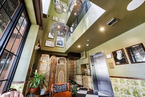 A hotel lobby with a high ceiling, large windows, a staircase, and a refrigerator.