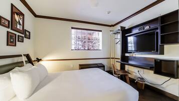 Een hotelkamer met een bed, een aan de muur bevestigde televisie, een raam met zonwering en aan de muur hangende foto's.
