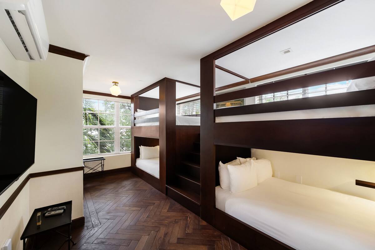 A room with bunk beds, a television, and a window with a view of greenery.