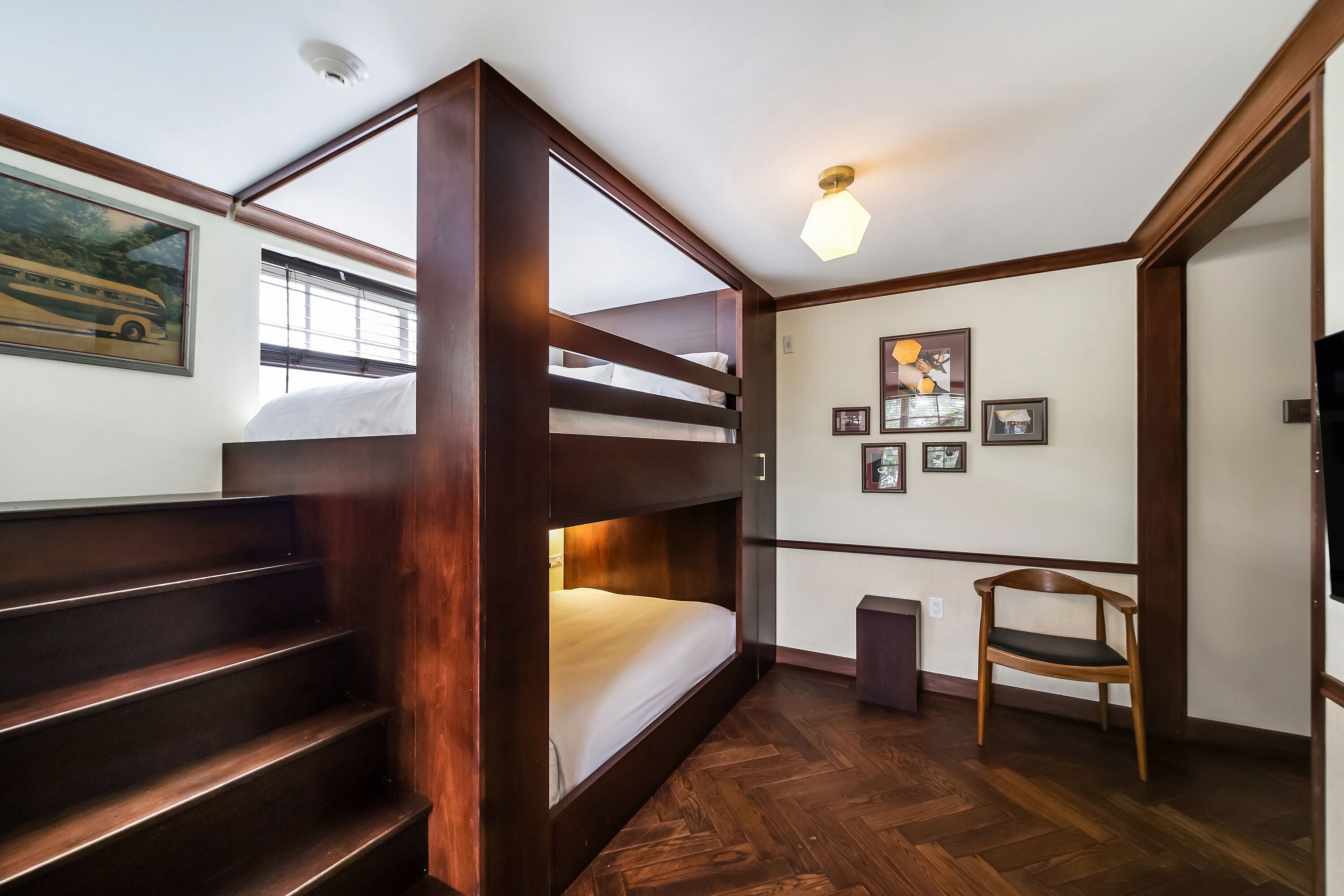 A bunk bed room with a wooden floor, a chair, and a wall with framed pictures.
