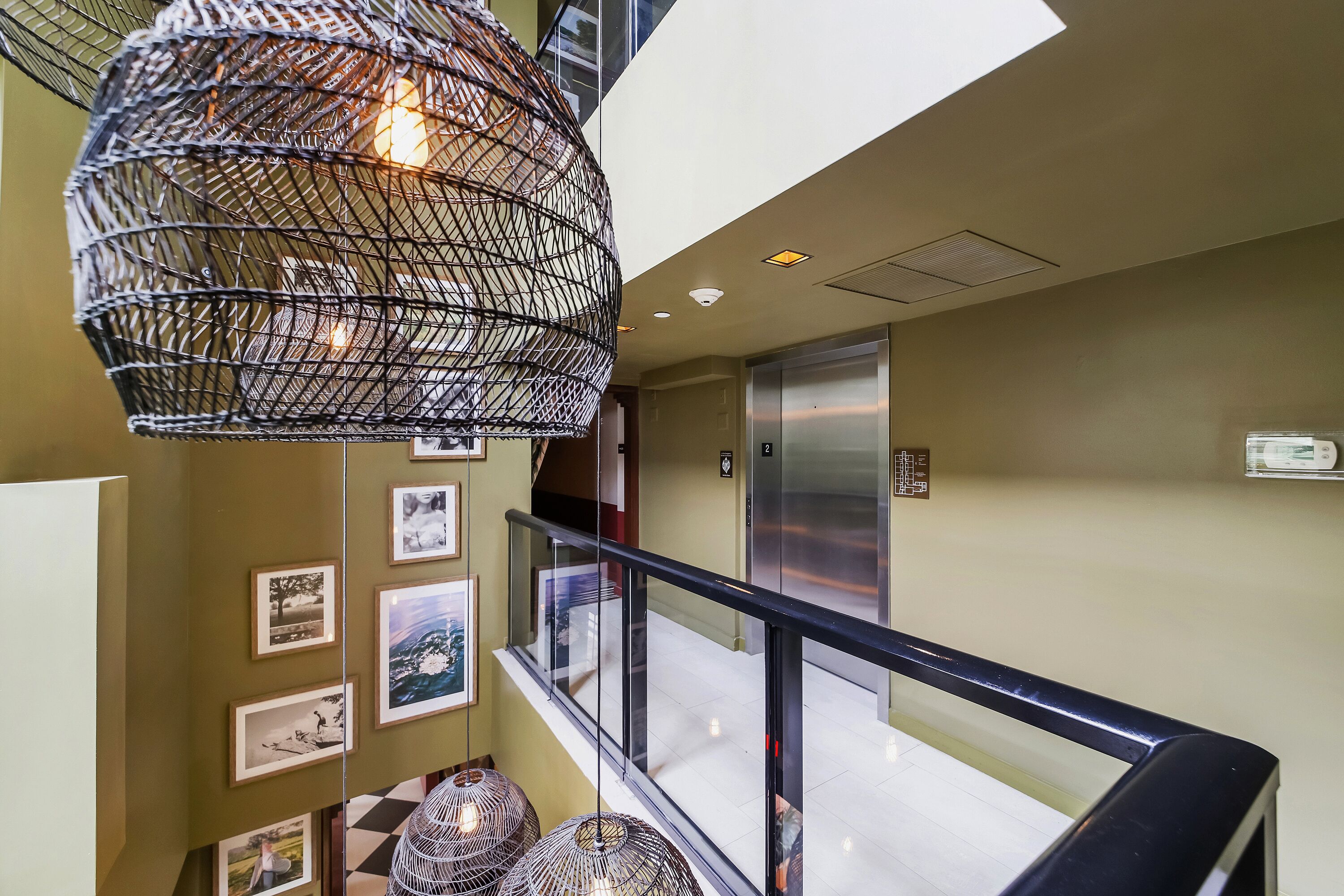 Um interior moderno com guarda-corpo de vidro, luminária pendente e quadros nas paredes.