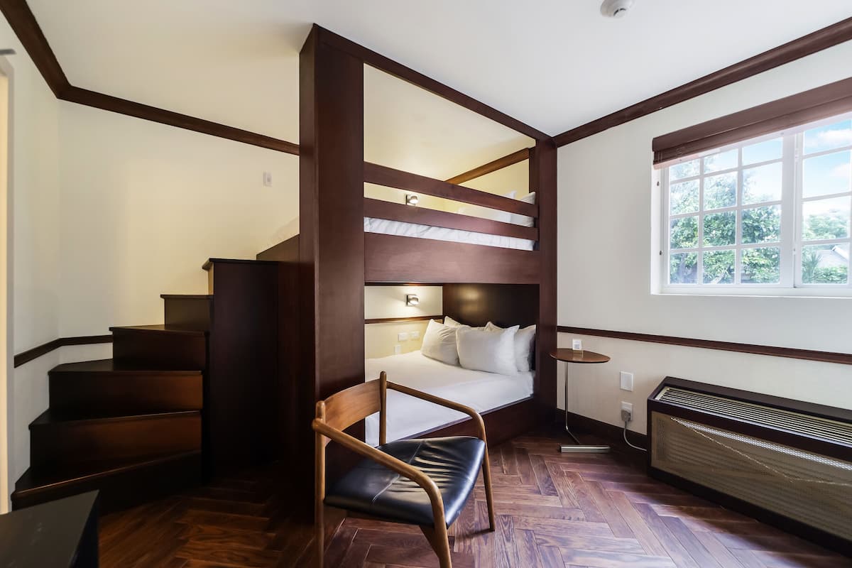 A room with a bunk bed, a chair, a heater, and a window with a view of greenery.