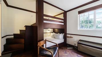 Ein Zimmer mit Etagenbett, Stuhl, Heizung und einem Fenster mit Blick ins Grüne.