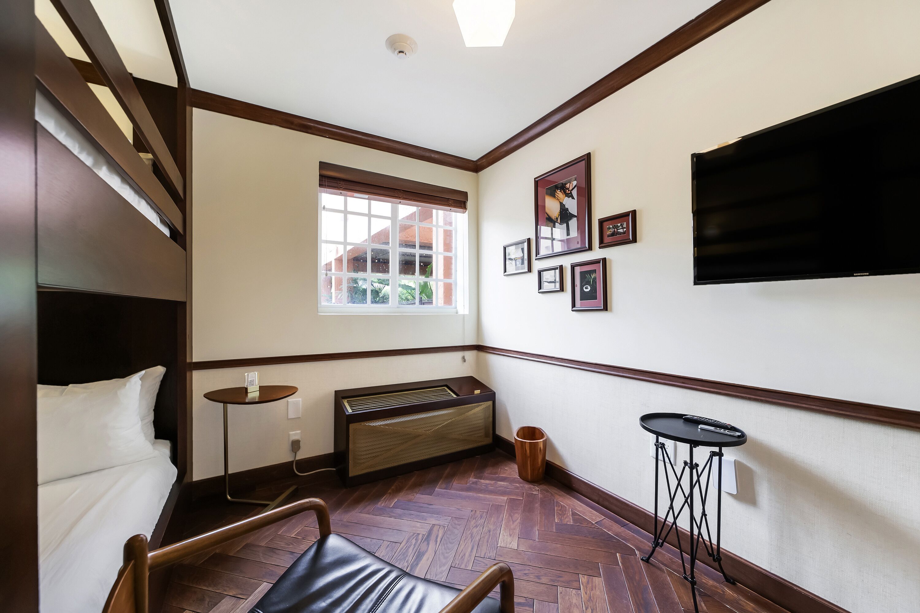 Habitación de hotel con cama, calefacción, ventana, televisor montado en la pared y una pequeña mesa.