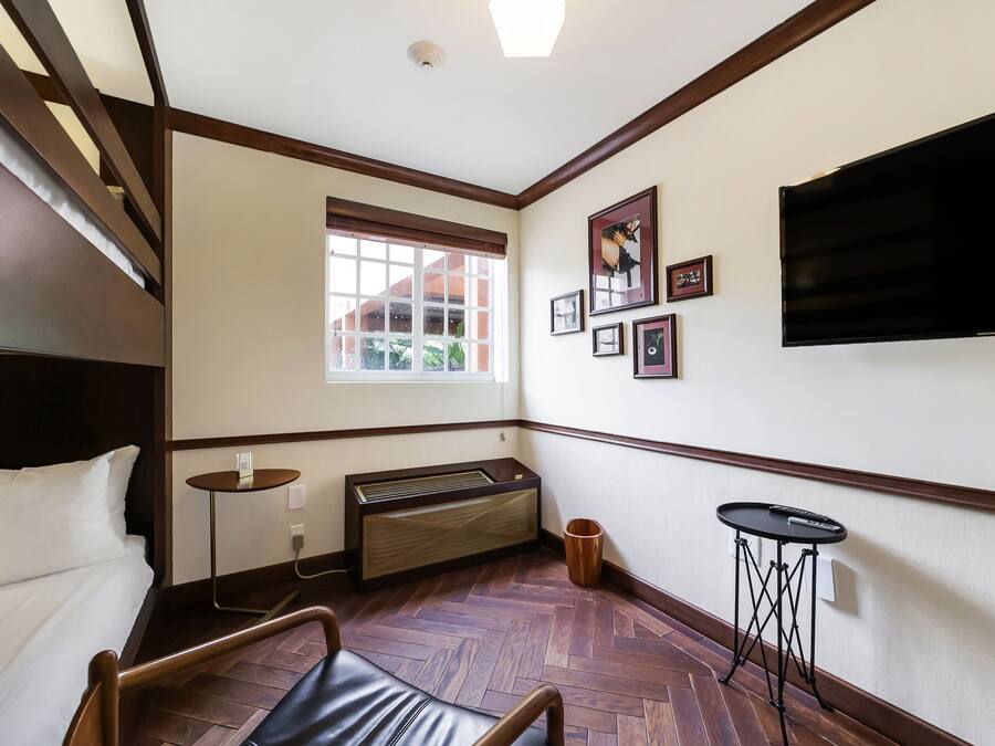Habitación de hotel con cama, calefacción, ventana, televisor montado en la pared y una pequeña mesa.