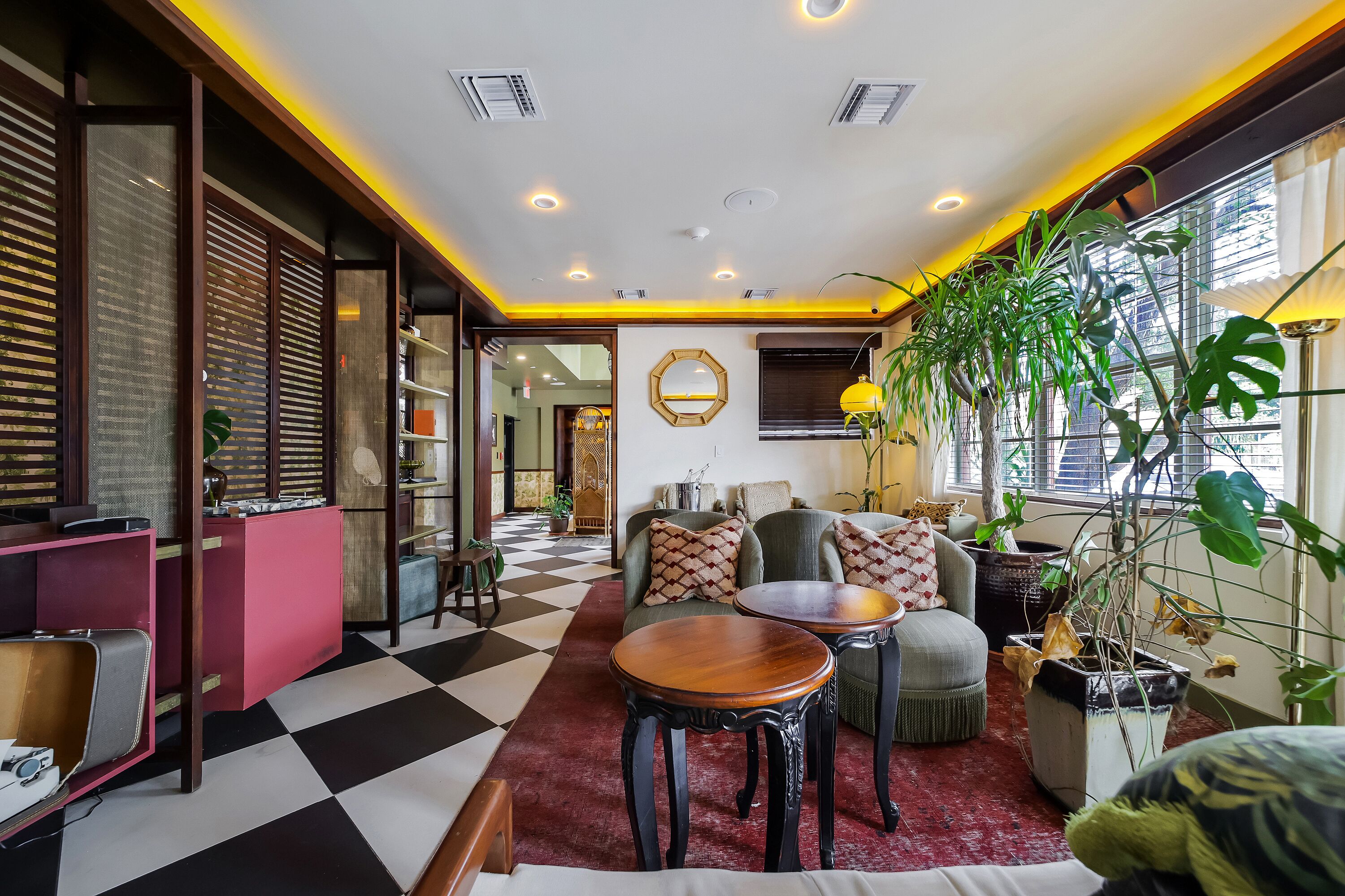 A room with a checkered floor, a sofa with cushions, a wooden table, and potted plants.