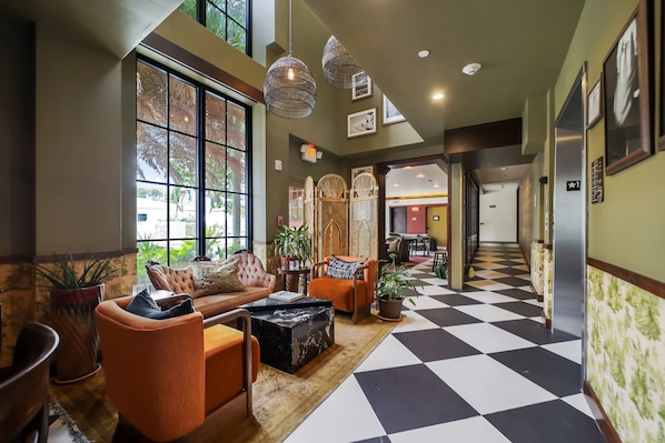 A hotel lobby with a checkered floor, seating area with sofas and armchairs, hanging light fixtures, and framed pictures on the walls.
