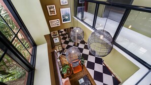 Um hall com pé-direito alto, piso xadrez, guarda-corpo de vidro e vista para a área externa.