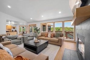 A spacious living area with a fireplace, large windows, and a view of greenery.