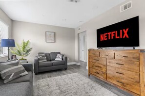 A living room with a grey sofa, a wooden cabinet, a TV displaying 'NETFLIX,' and a potted plant. - Welcome to Serene Sunshine Retreat Spring Hill, FL (Spring Hill)
