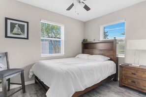 A bedroom with a bed, a nightstand, a chair, and two windows with blinds. - Welcome to Serene Sunshine Retreat Spring Hill, FL (Spring Hill)