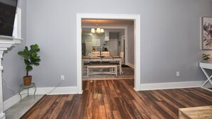 Ein Zimmer mit Holzboden, einem Esstisch mit Stühlen, einer Topfpflanze und einem Bild an der Wand.