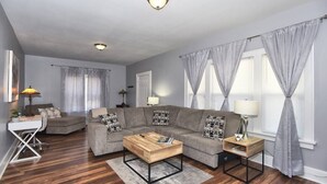 Ein modernes Wohnzimmer mit einer Eckcouch, einem Couchtisch, einem Schreibtisch und einer Lampe.
