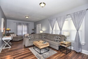 A modern living room with a sectional sofa, a coffee table, a desk, and a lamp. - NEW- LUXURY CHERRY ST -SHOP DINE -2 BEDROOM HOUSE-HOSPITALS-RT 66--DOWNTOWN (TULSA)