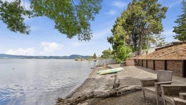 Un patio frente al lago con sillas, una fogata y una terraza de madera con vista al agua.