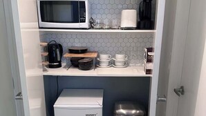 Una kitchenette compacta equipada con microondas, cafetera y refrigerador pequeño.