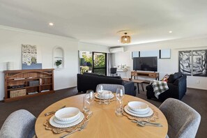 Un salon moderne avec une table à manger ronde pour quatre personnes, un canapé noir, un téléviseur et une bibliothèque.