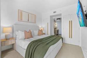 A modern hotel room with a large bed, bedside lamps, a green throw blanket, a flat-screen TV, and a wardrobe with gold handles.