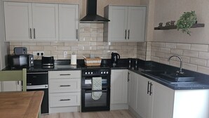 Una cocina con gabinetes blancos, una encimera negra, una estufa, un microondas y un lavabo.