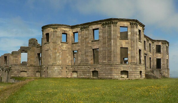 An old, circular stone building with multiple windows and a grassy field in the foreground.