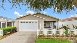 Einbungalow mit Garage, überdachter Veranda und weißem Zaun.