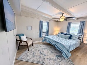 Ein Schlafzimmer mit Bett, Stuhl, Deckenventilator und einem Fenster mit Vorhängen.