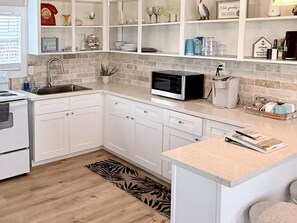 Eine moderne Küche mit weißen Schränken, einer Mikrowelle, einem Spülbecken und einer Arbeitsfläche mit Wasserkocher und Toaster.