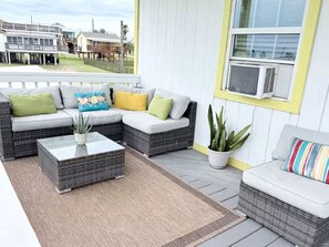 A covered outdoor seating area with wicker furniture, a potted plant, and a view of a residential neighborhood. - Surfside Beach House • Walk to Sand and Fish • Sleeps 8 • Pet Friendly (Surfside Beach)