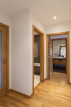A hallway with wooden flooring, a bathroom with a mirror and sink, and a door leading to another room. - Colinas Premium 3BR - Three Bedroom Apartment, Sleeps 5 (Sintra)