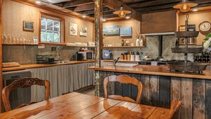 Una cocina rústica con encimeras de madera, una mesa de comedor y sillas. Hay copas de vino en la encimera, un reloj en la pared y una ventana con vistas.