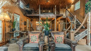 Un interior rústico con entrepiso, escalera de madera y comedor con muebles antiguos.