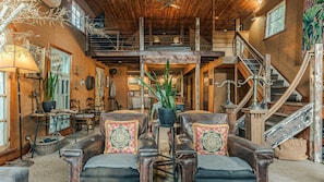 Un interior rústico con entrepiso, escalera de madera y comedor con muebles antiguos.
