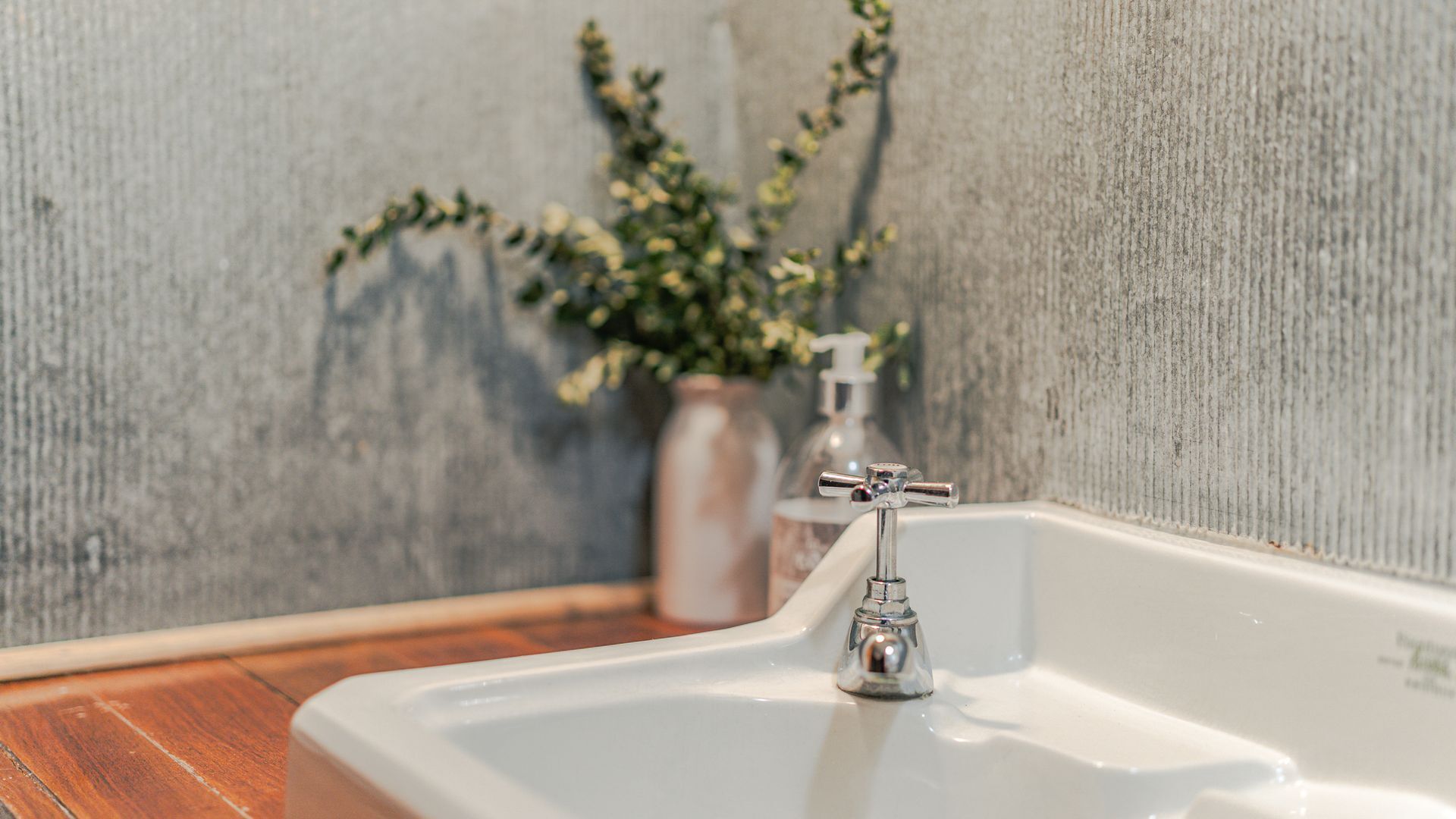 Une salle de bain avec un lavabo blanc, un robinet chromé, un distributeur de savon et un vase avec des fleurs accroché au mur.