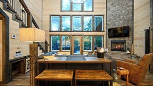 A spacious living area with a fireplace, large windows, and a staircase. - Retreat w/ Sauna, Hot Tub, Games & Fenced Dog Yard! (Broken Bow)
