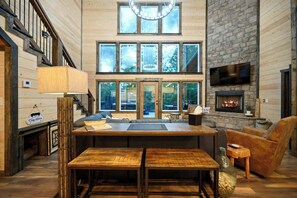 A spacious living area with a fireplace, large windows, and a staircase. - Retreat w/ Sauna, Hot Tub, Games & Fenced Dog Yard! (Broken Bow)