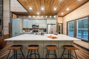 A modern kitchen with a large island, bar stools, and a brick wall. - Retreat w/ Sauna, Hot Tub, Games & Fenced Dog Yard! (Broken Bow)