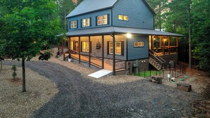 A two-story house with a porch, a staircase leading to the upper level, and a gravel driveway. - Retreat w/ Sauna, Hot Tub, Games & Fenced Dog Yard! (Broken Bow)