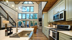 A modern kitchen with a large island, stainless steel appliances, and a stone fireplace. - Retreat w/ Sauna, Hot Tub, Games & Fenced Dog Yard! (Broken Bow)