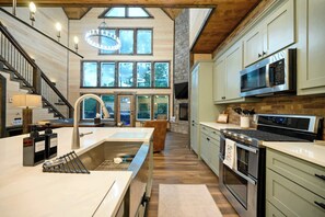 A modern kitchen with a large island, stainless steel appliances, and a stone fireplace. - Retreat w/ Sauna, Hot Tub, Games & Fenced Dog Yard! (Broken Bow)