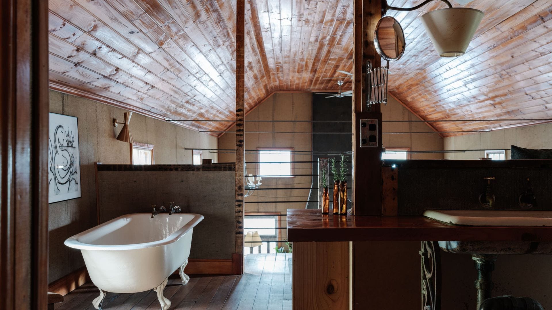 Une salle de bain rustique avec une baignoire sur pieds d’époque, des poutres en bois au plafond et une fenêtre laissant entrer la lumière naturelle.
