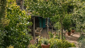 Ein Garten mit Topfpflanzen, Korbmöbeln und einer Holzhütte mit grünen Fensterläden.