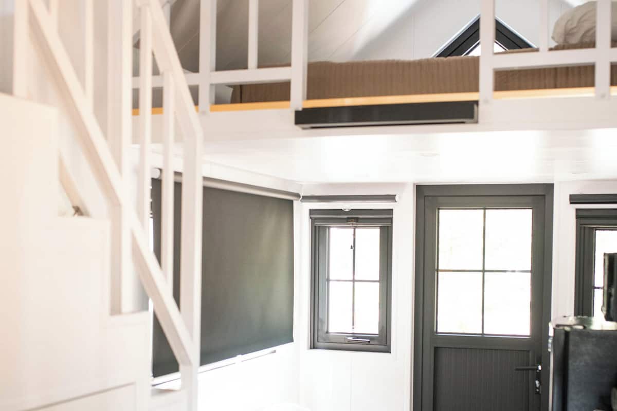 A compact, modern room with a loft bed, a sofa, a desk, and a door.