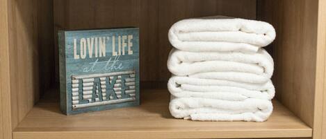 A wooden shelf with a sign, towels, a framed picture, and small potted plants.