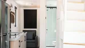 Una cocina compacta con refrigerador empotrado, un sofá gris y una escalera que sube a un nivel superior.
