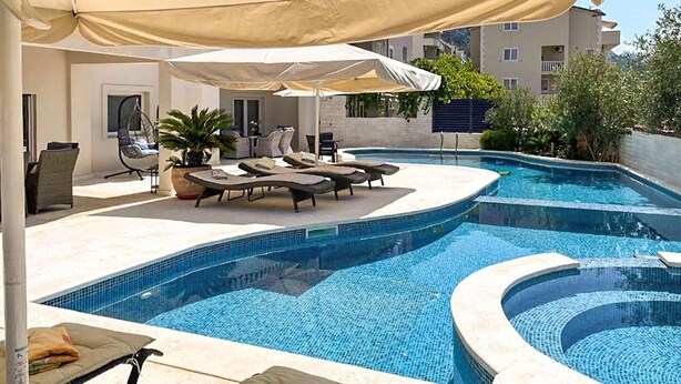Ein Pool mit Liegestühlen und Sonnenschirmen, umgeben von einem Gebäude mit Kachelfassade.