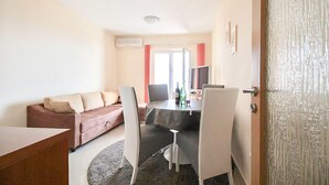 Ein Zimmer mit einer Couch, einem Esstisch mit Stühlen, einem Fernseher und einer Tür.