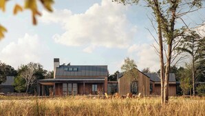 A modern house with a large window, a chimney, and a wooden deck. - Hideaway Round Top | Full Property | 21-Acre Luxury Estate (Round Top)