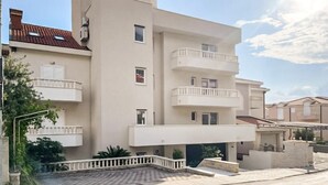 Un immeuble résidentiel à plusieurs étages, doté de balcons, d’une cour pavée et surplombant un ciel dégagé.