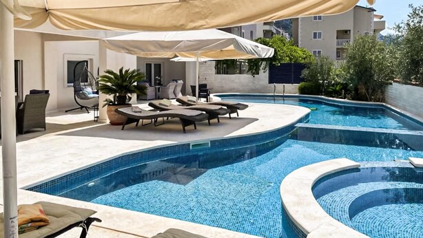 Une piscine entourée de chaises longues et de parasols, elle-même bordée d’un bâtiment dont la façade est recouverte de carreaux.