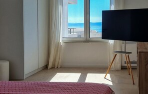 Ein Schlafzimmer mit großem Fenster, einem Bett, einem Fernseher und einem kleinen Hocker.